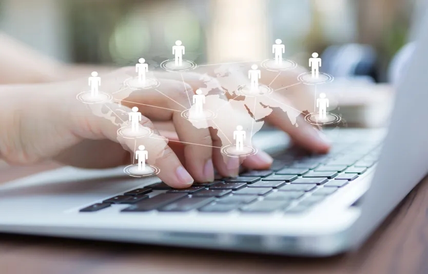 Hands typing on a laptop keyboard with global network icons and world map.