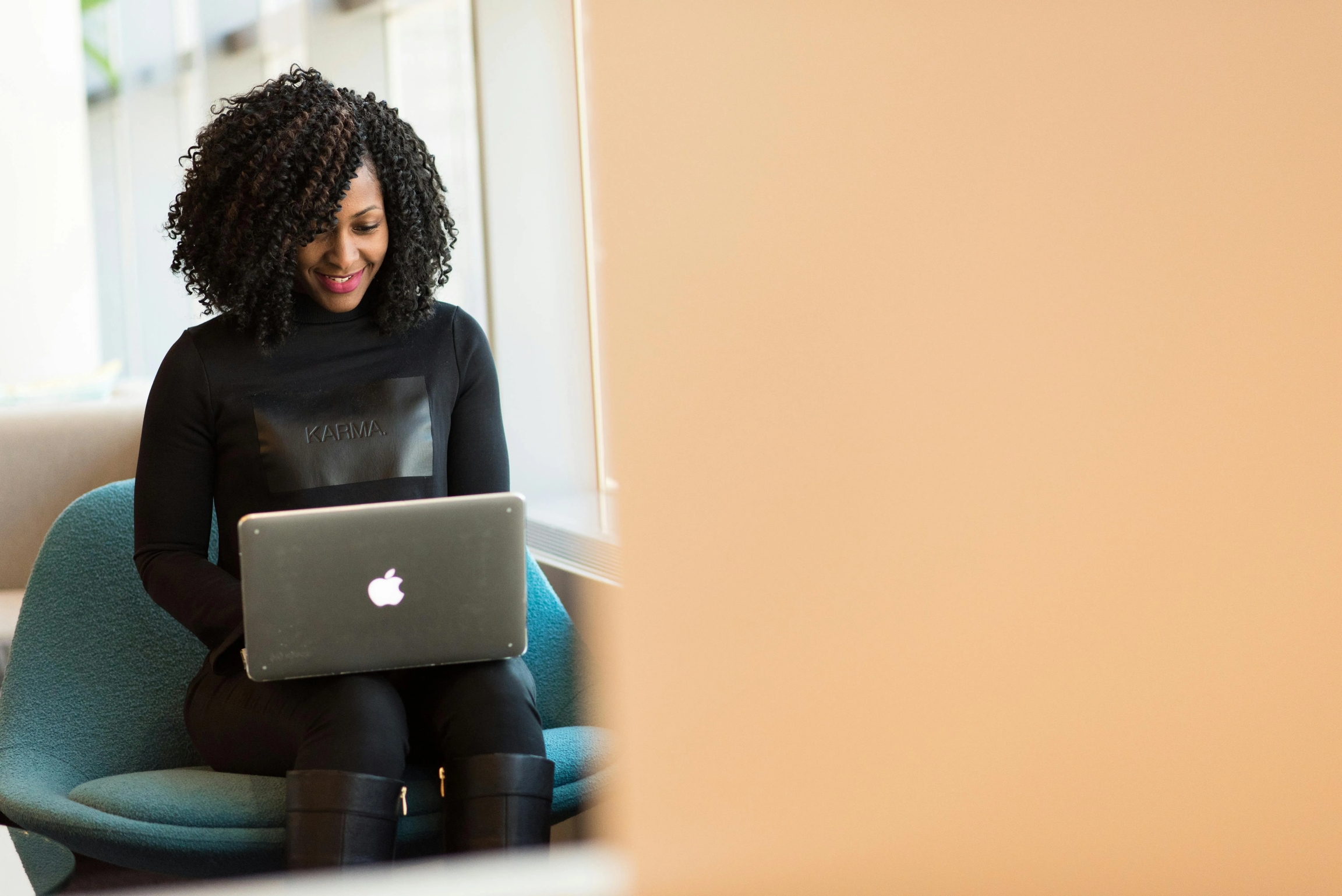 Professional woman in Karma apparel smiling while using silver MacBook laptop.