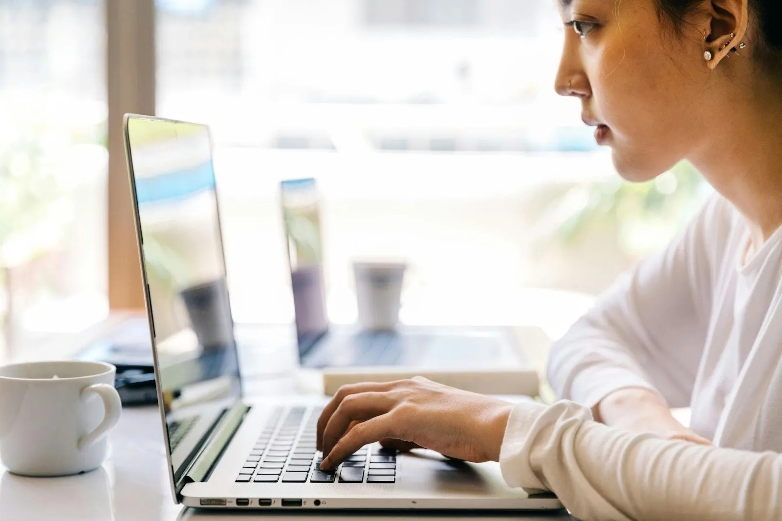 Young woman working remotely on silver laptop in bright modern cafe.