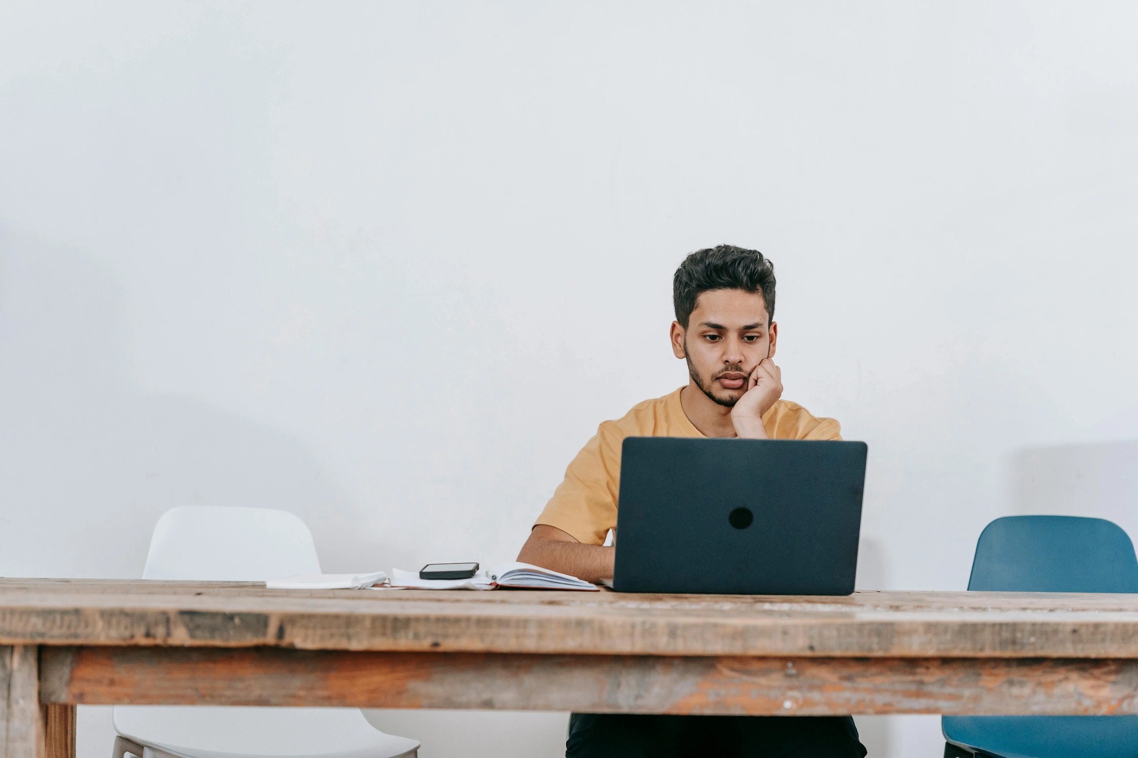 Young man focused on working remotely with laptop on a wooden table.