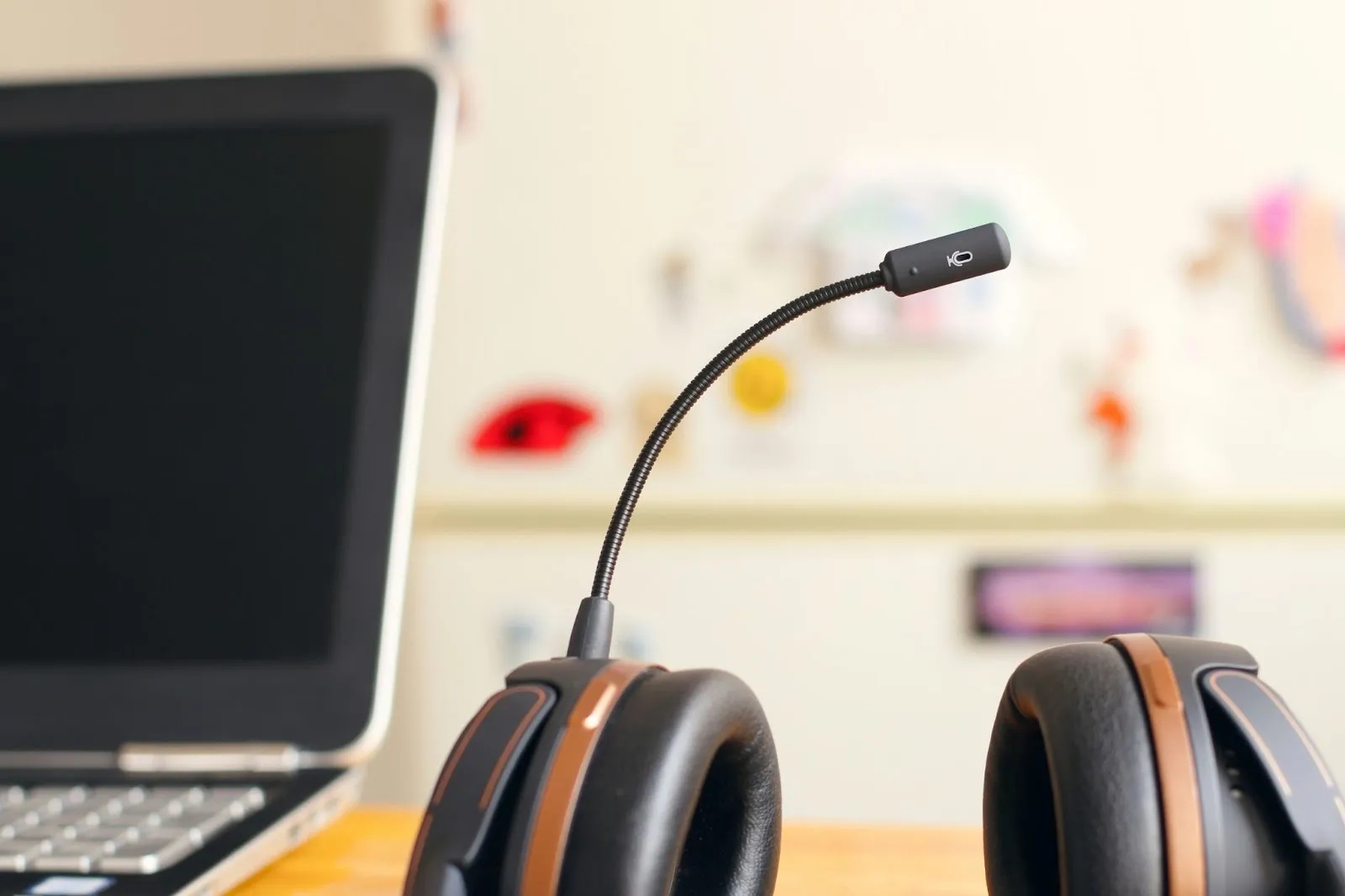 Gaming headset with flexible microphone on wooden desk, silver laptop in background.