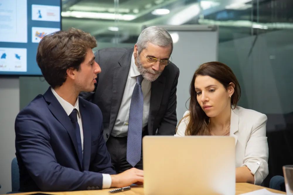 Business team collaborating in office with laptop and screen.